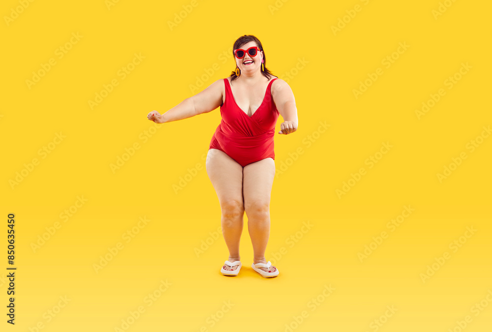 Portrait of a funny happy fat overweight woman in red swimsuit ready for summer holiday trip and having fun dancing on a yellow studio background. Vacation, journey and travelling concept. Portrait of a funny happy fat overweight woman in red swimsuit ready for summer holiday trip and having fun dancing on a yellow studio background. Vacation, journey and travelling concept.