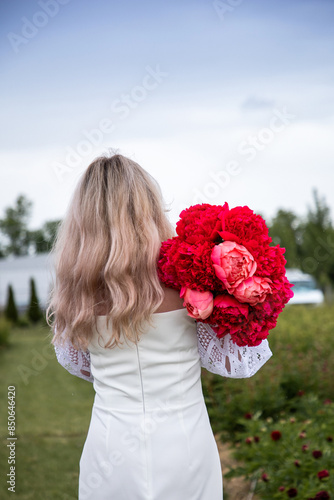 Girl with a bouquet of peony. A field of peonies. A woman in a white dress. Red peony flowers