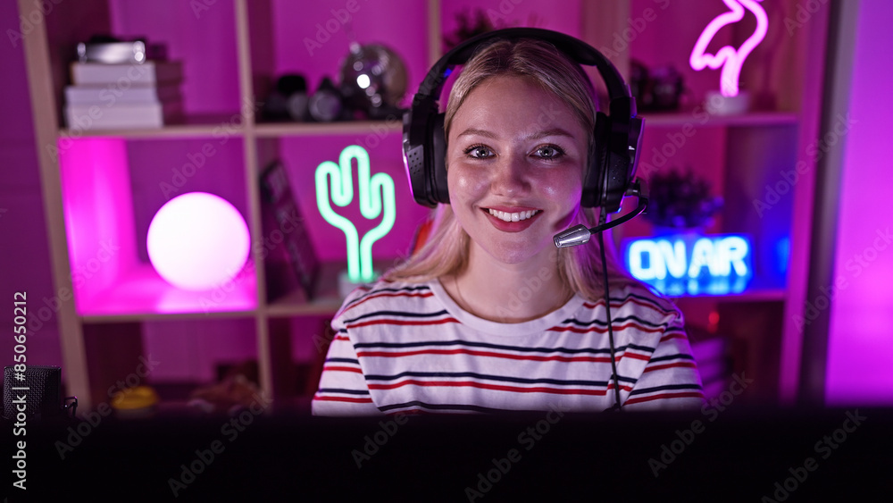 A smiling young woman with headphones in a neon-lit gaming room at night. A smiling young woman with headphones in a neon-lit gaming room at night.