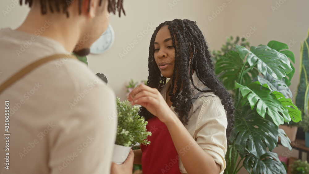 A woman florist assists a male customer in a lush indoor flower shop filled with green plants.