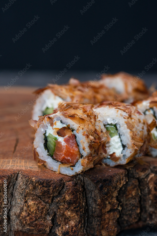 Sushi roll with salmon, cucumber, avocado and tuna shavings on a wooden board Sushi roll with salmon, cucumber, avocado and tuna shavings on a wooden board