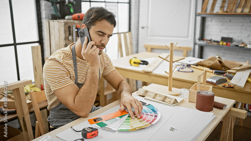 Handsome hispanic man on phone choosing colors in a sunny carpentry workshop Handsome hispanic man on phone choosing colors in a sunny carpentry workshop