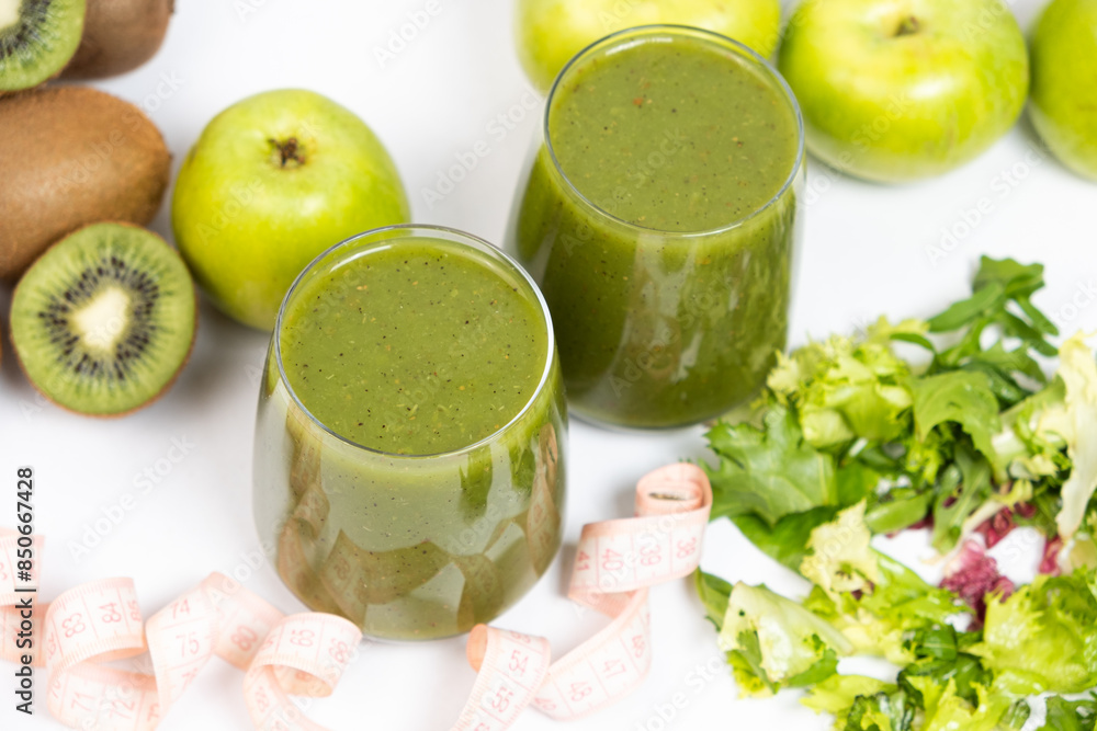 A green smoothie in a glass and a measuring tape. A healthy drink for weight loss A green smoothie in a glass and a measuring tape. A healthy drink for weight loss
