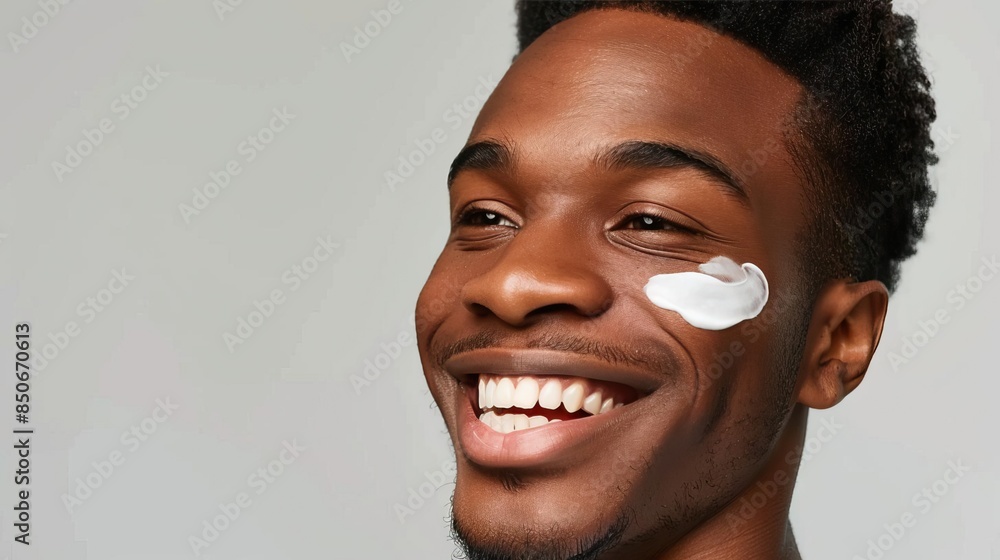 A man with a bright smile and facial cream applied to his cheek A man with a bright smile and facial cream applied to his cheek