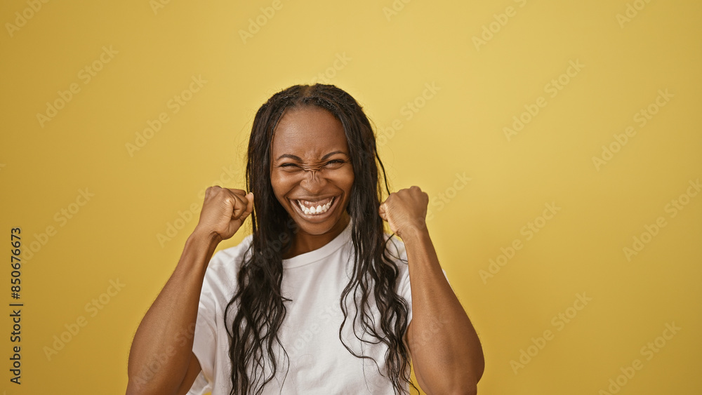 Fototapeta premium An overjoyed young woman with curly hair celebrates excitedly against a yellow background.
