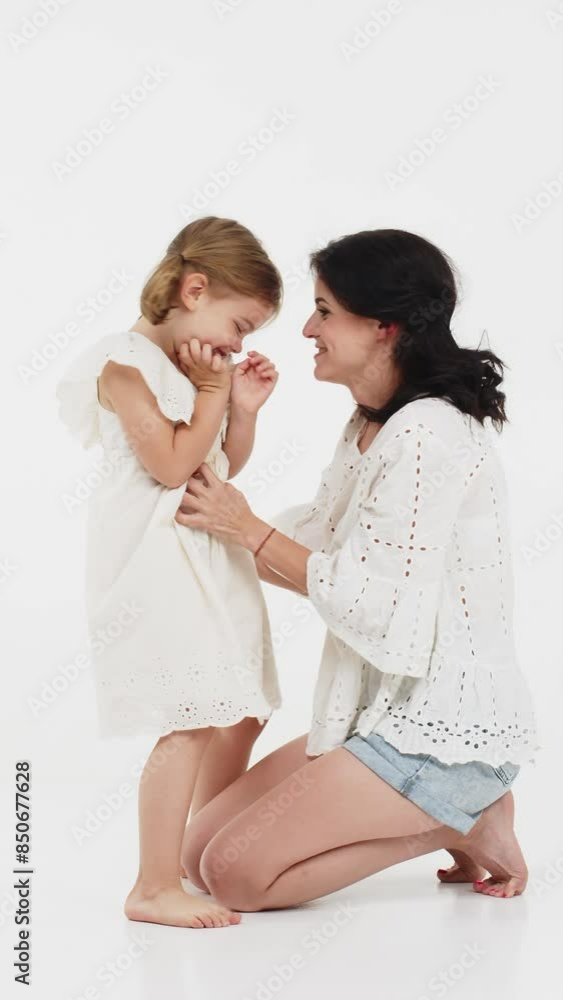 Vertical video. A mother woman in light clothes has fun with a cute little girl. Mother and little daughter isolated on white background. Mother's day, love, family, parenthood, childhood concept. Vertical video. A mother woman in light clothes has fun with a cute little girl. Mother and little daughter isolated on white background. Mother's day, love, family, parenthood, childhood concept.