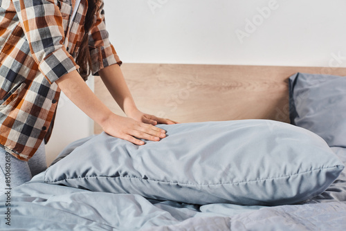 A person, likely a girl, gently lays a pillow on a neatly made bed in a warm, inviting bedroom.