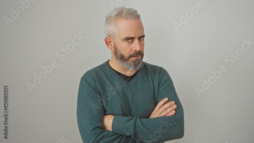 Portrait of a pensive mature caucasian man with arms crossed against a white background.