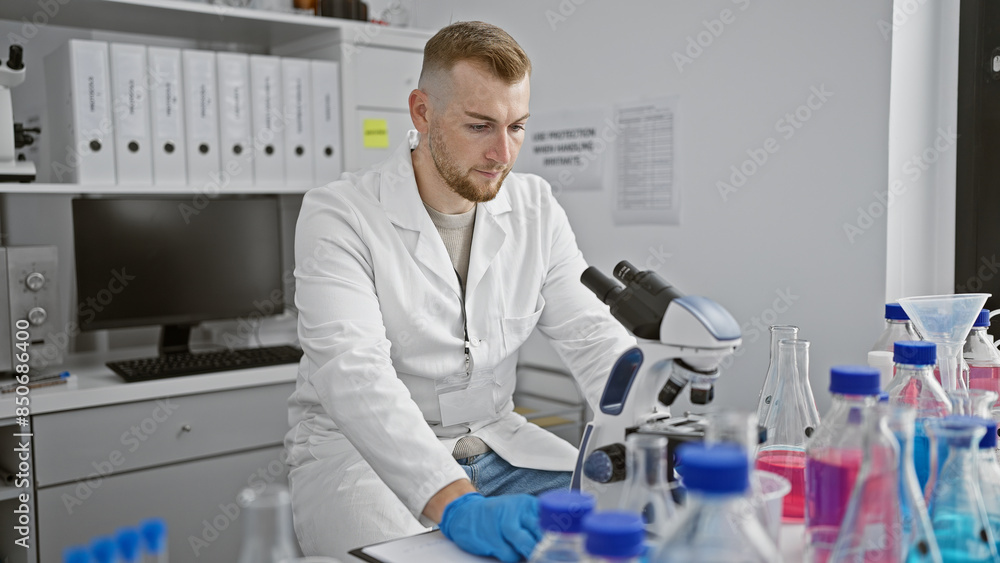 A young caucasian man focuses on a microscope in a modern laboratory setting, surrounded by scientific equipment. A young caucasian man focuses on a microscope in a modern laboratory setting, surrounded by scientific equipment.