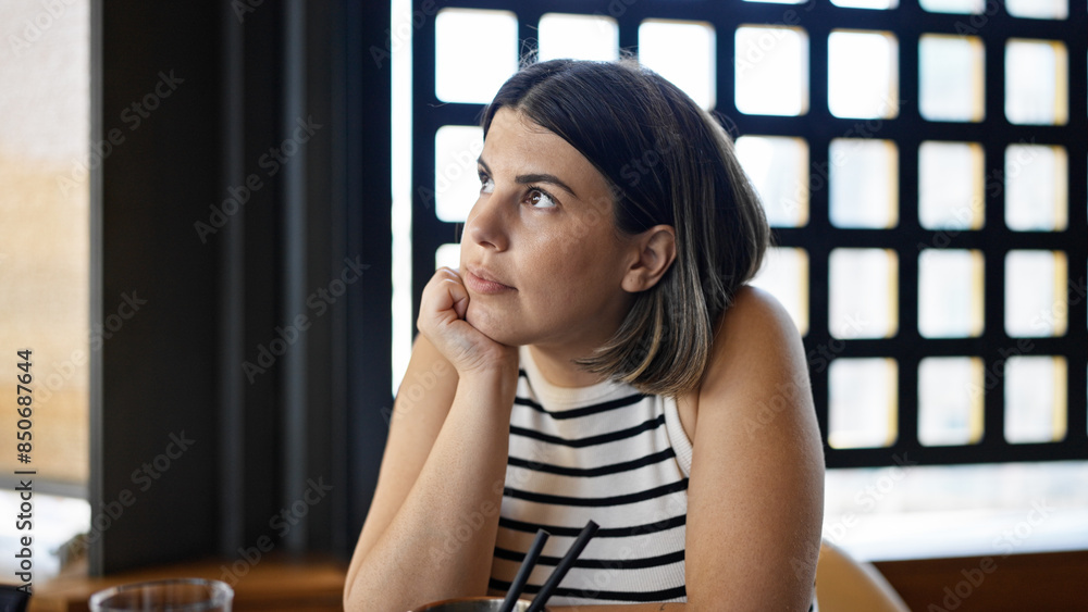 Young beautiful hispanic woman sitting on the table looking serious at the restaurant Young beautiful hispanic woman sitting on the table looking serious at the restaurant