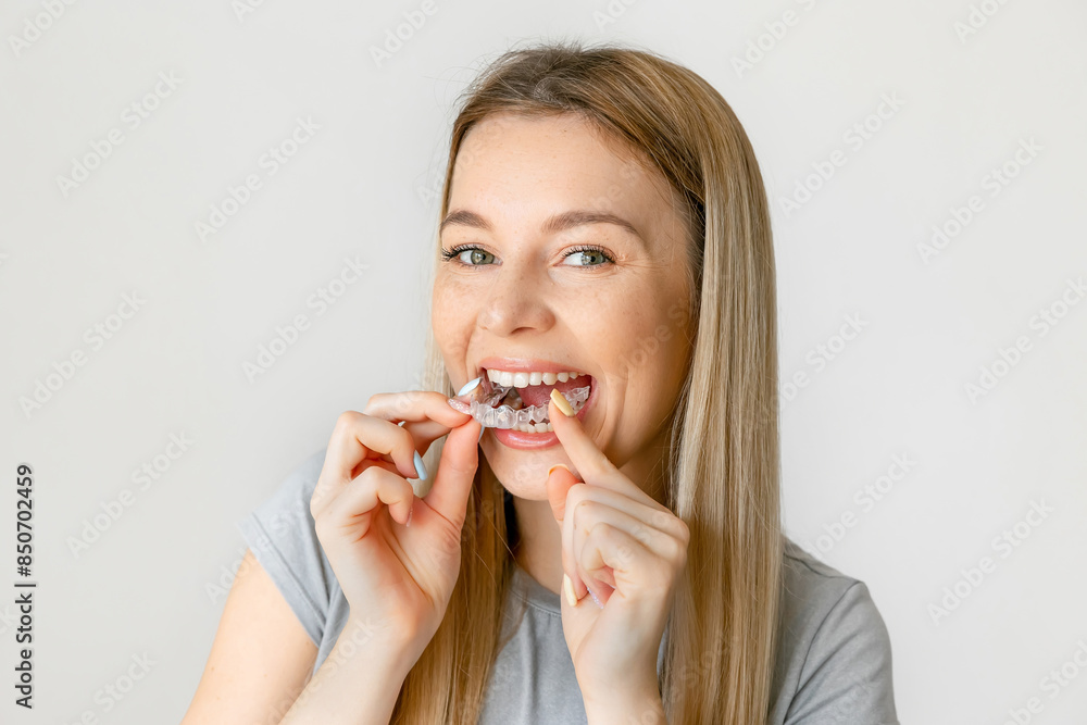 Attractive young woman puts a dental retainer on her teeth, she stands on a white background. Orthodontist. Dental tray. Retainer. Place for an inscription. Attractive young woman puts a dental retainer on her teeth, she stands on a white background. Orthodontist. Dental tray. Retainer. Place for an inscription.