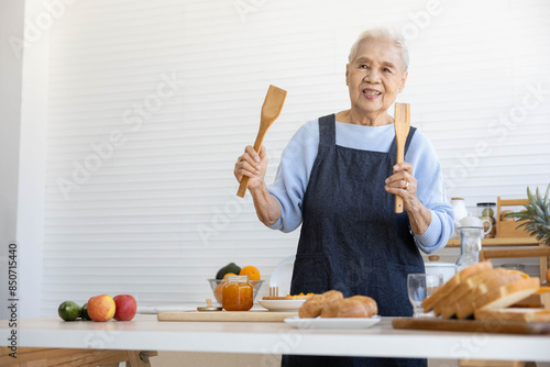 senior woman or housewife holding and showing wooden spatula in the kitchen photo