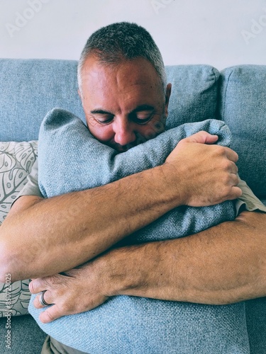 Принти на полотні Young adult man sitting on sofa hugging pillow