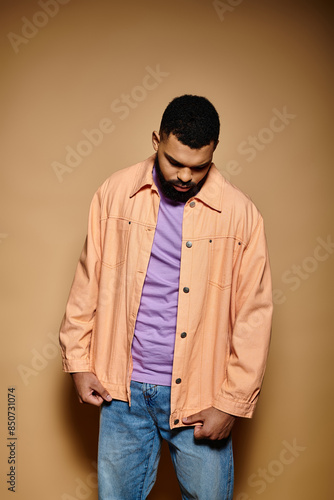 Handsome African American man in fashionable attire standing with hands in pockets in front of vibrant backdrop.