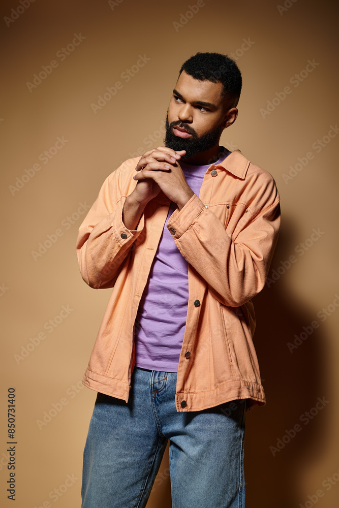 Fototapeta premium Fashionable African American man poses against a striking brown wall.