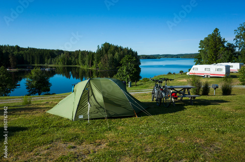 Green tent on a campsite grass, Bicycles stand next to a wooden picnic table, Sunny day blue sky, lake Ärtingen, Bengtsfors, Sweden