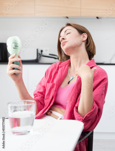 Tired and overheated attractive woman suffering from a heat attack uses an electric handy fan to cool herself down in a hot summer day