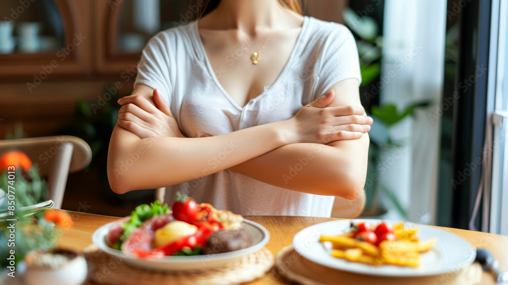 Woman making crossed arms hand sign to refuse food at a dining table, indicating rejection or dislike Woman making crossed arms hand sign to refuse food at a dining table, indicating rejection or dislike