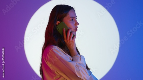 Stylish young woman in casual clothing calling talking on smartphone. Isolated on colorful studio background spotlight. photo