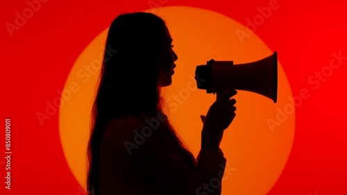 Stylish young woman black silhouette in casual clothing speaking in loud speaker advertising product. Isolated on red studio background spotlight. photo