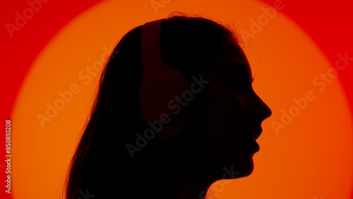 Stylish young woman black silhouette listening music in headphones, face close up. Isolated on red studio background spotlight. photo