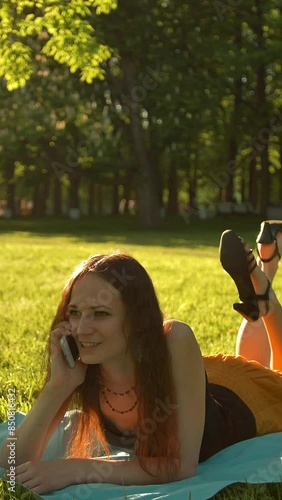 Pretty girl lying down on a meadow and talking by smartphone. She very happy of conversetion vith friend. Sunset. 4k ultraHD. Vertical shot. photo