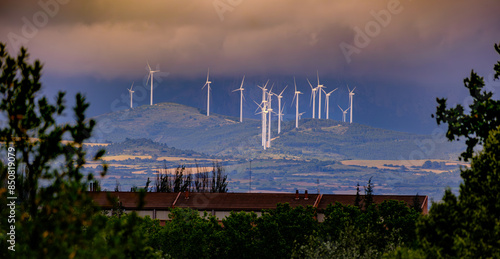 This image showcases a wind farm set against a cloudy sky, with numerous wind turbines strategically placed on a hill. The turbines are generating clean, renewable energy, highlighting the importance 