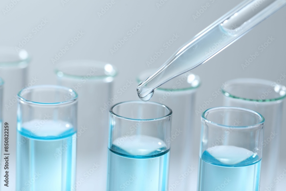 Dripping liquid from pipette into test tube on light background, closeup Dripping liquid from pipette into test tube on light background, closeup
