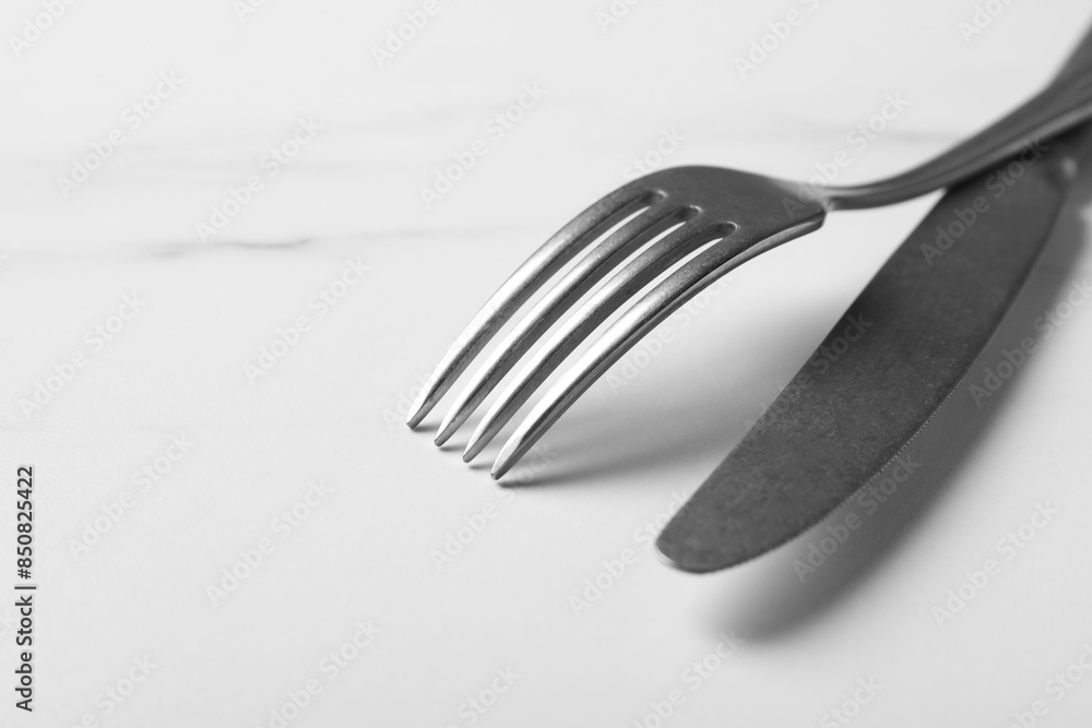 Stylish cutlery. Silver knife and fork on white marble table, closeup. Space for text Stylish cutlery. Silver knife and fork on white marble table, closeup. Space for text