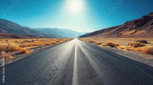 Empty asphalt road, winding through vast desert, clear blue sky, wideangle shot, bright sunlight, crisp details © Karn AS Images