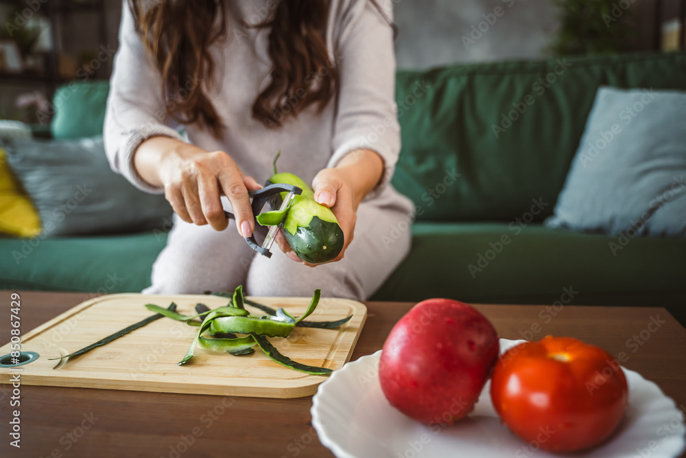 Unknown adult caucasian woman sit and peel a cucumber at home Unknown adult caucasian woman sit and peel a cucumber at home