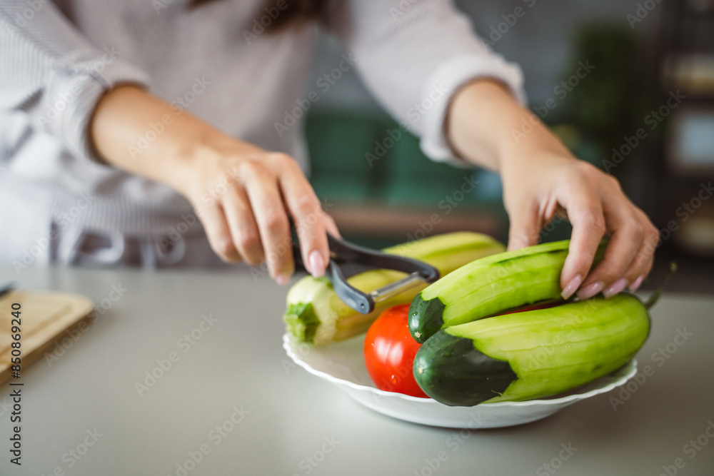 Unknown adult caucasian woman stand and peel a cucumber at home Unknown adult caucasian woman stand and peel a cucumber at home
