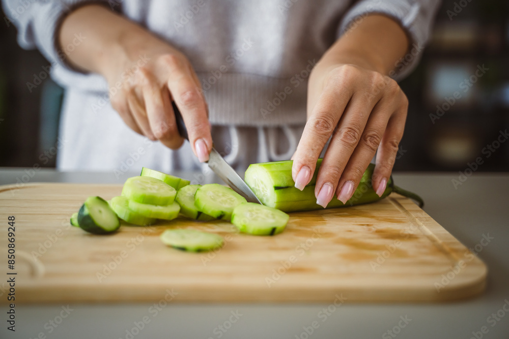 An unknown adult caucasian woman stand and cut cucumber at home An unknown adult caucasian woman stand and cut cucumber at home