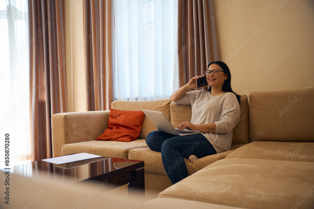 Joyous adult woman with laptop communicating on smartphone Joyous adult woman with laptop communicating on smartphone