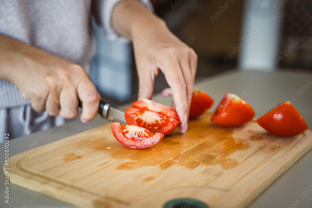 An unknown woman stand and cut tomato with knife on table at home An unknown woman stand and cut tomato with knife on table at home