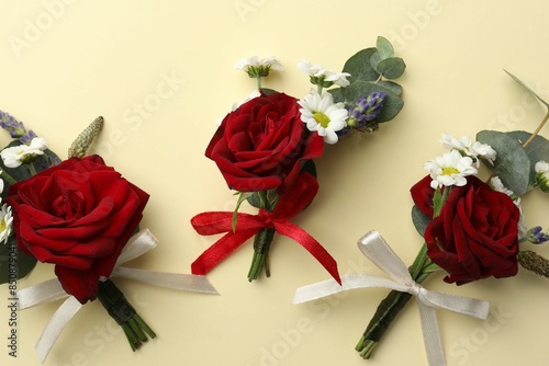 Many stylish red boutonnieres on beige background, flat lay photo