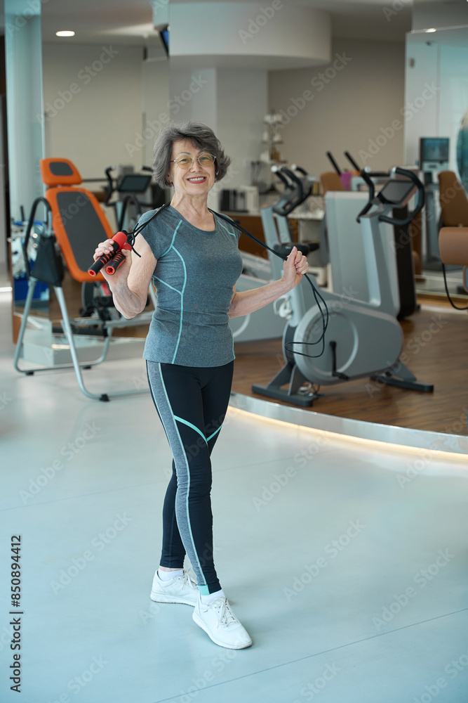 Fototapeta premium Elderly lady stands with a jump rope in a gym