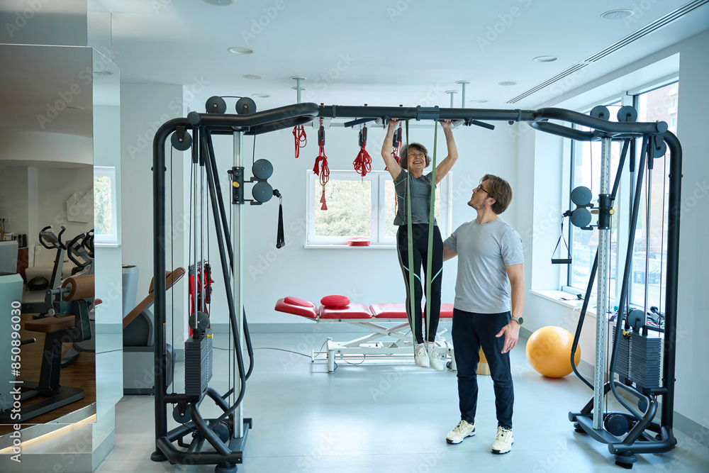 Fototapeta premium Rehabilitologist works with an elderly woman on a suspension system