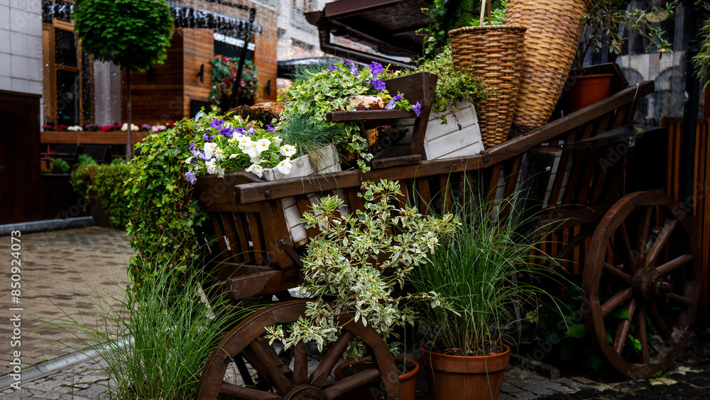 Fototapeta premium a quaint urban alleyway enhanced with rustic wooden carts overflowing with an array of vibrant flowers and plants, creating a charming and green atmosphere.