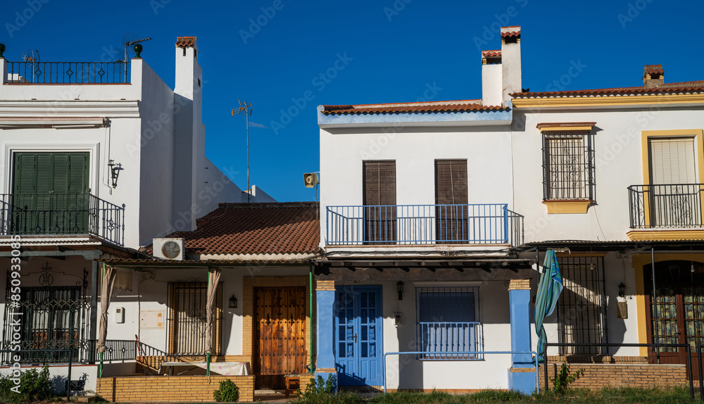 a row of charming traditional Andalusian townhouses, with white walls and terracotta roofs, featuring colorful doors and wrought-iron balconies under a clear, vivid blue sky a row of charming traditional Andalusian townhouses, with white walls and terracotta roofs, featuring colorful doors and wrought-iron balconies under a clear, vivid blue sky