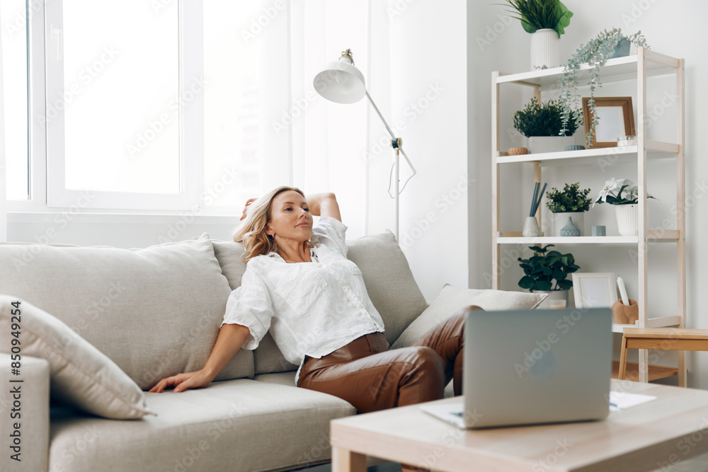 Woman working remotely on laptop, seated on couch with coffee table, cozy home office environment Woman working remotely on laptop, seated on couch with coffee table, cozy home office environment