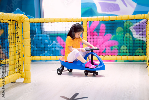 A child is having fun playing riding with a blue toy car, a cute Asian girl plays in an indoor playground. Children aged 7 years. photo