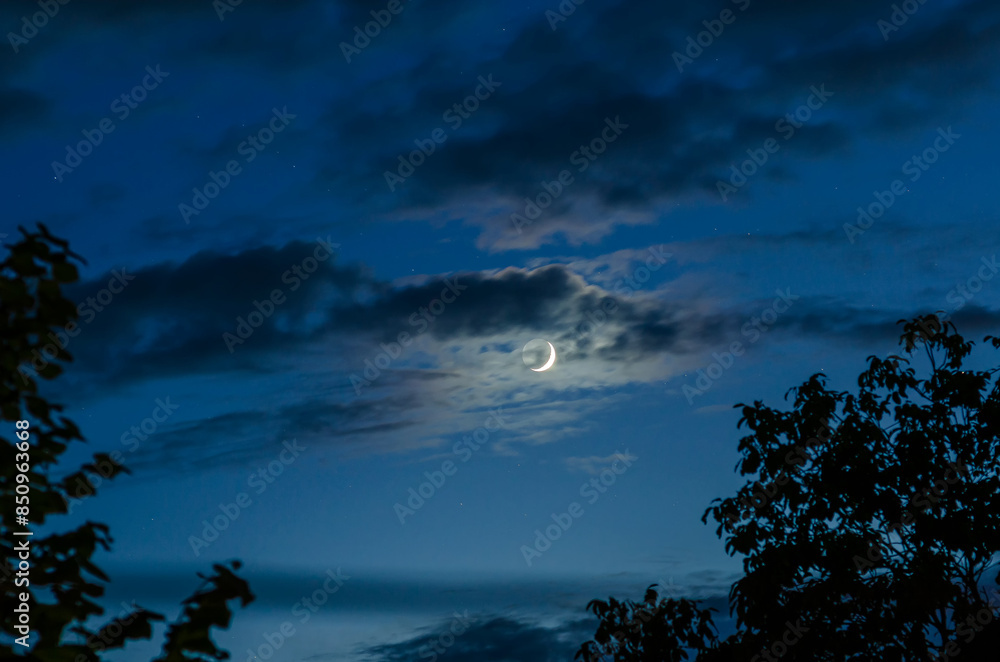New moon in blue sky with small clouds New moon in blue sky with small clouds