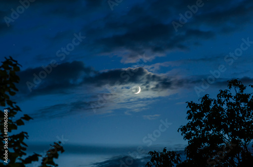 New moon in blue sky with small clouds © romankrykh