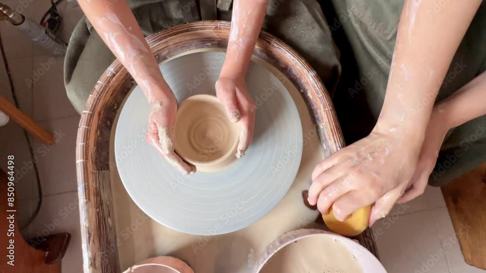 Making a handmade clay pot in the workshop. Pottery lesson with master. The hands of child work on a potter's wheel and make a pot from clay. A potter teaches a child pottery, making a clay jug.