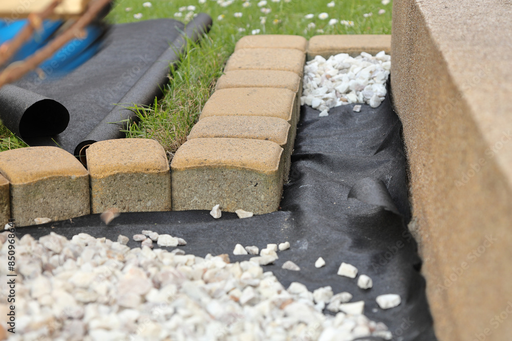 Laying an anti-weed mat in the garden together with paving stones and decorative pebbles Laying an anti-weed mat in the garden together with paving stones and decorative pebbles