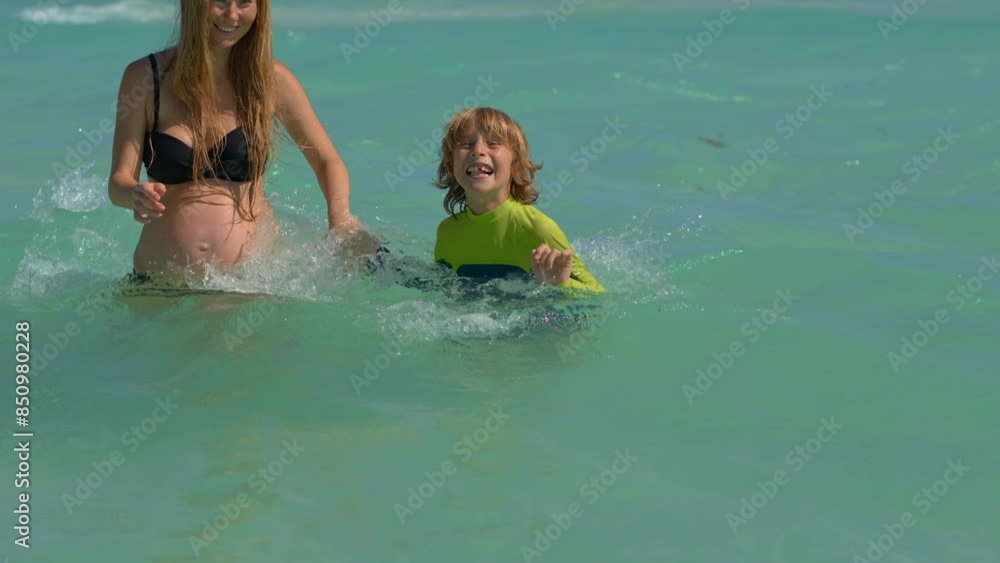 A pregnant woman and her elder son are enjoying a beautiful day at the beach with clear blue water. They laugh and play in the sand, creating cherished memories. Slowmotion video. A pregnant woman and her elder son are enjoying a beautiful day at the beach with clear blue water. They laugh and play in the sand, creating cherished memories. Slowmotion video.