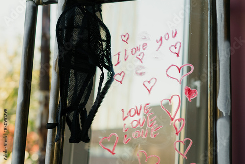 sexy girl writes a love message on the mirror and glass with red lipstick. The phrase I love you on the first date of a man and a woman. Erotic and romantic atmosphere with hearts and black lace bra
