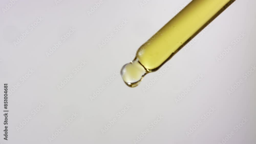 Close up of oil dropping from a dropper on isolated white background Close up of oil dropping from a dropper on isolated white background