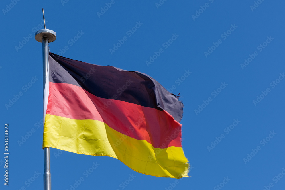 View of the national flag of Germany against a blue sky View of the national flag of Germany against a blue sky